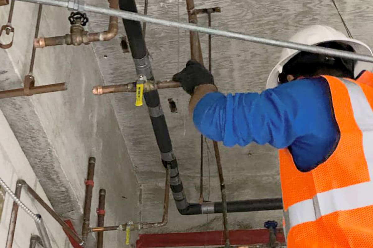Commercial plumber installing copper water supply pipes and overhead plumbing lines at a construction site.