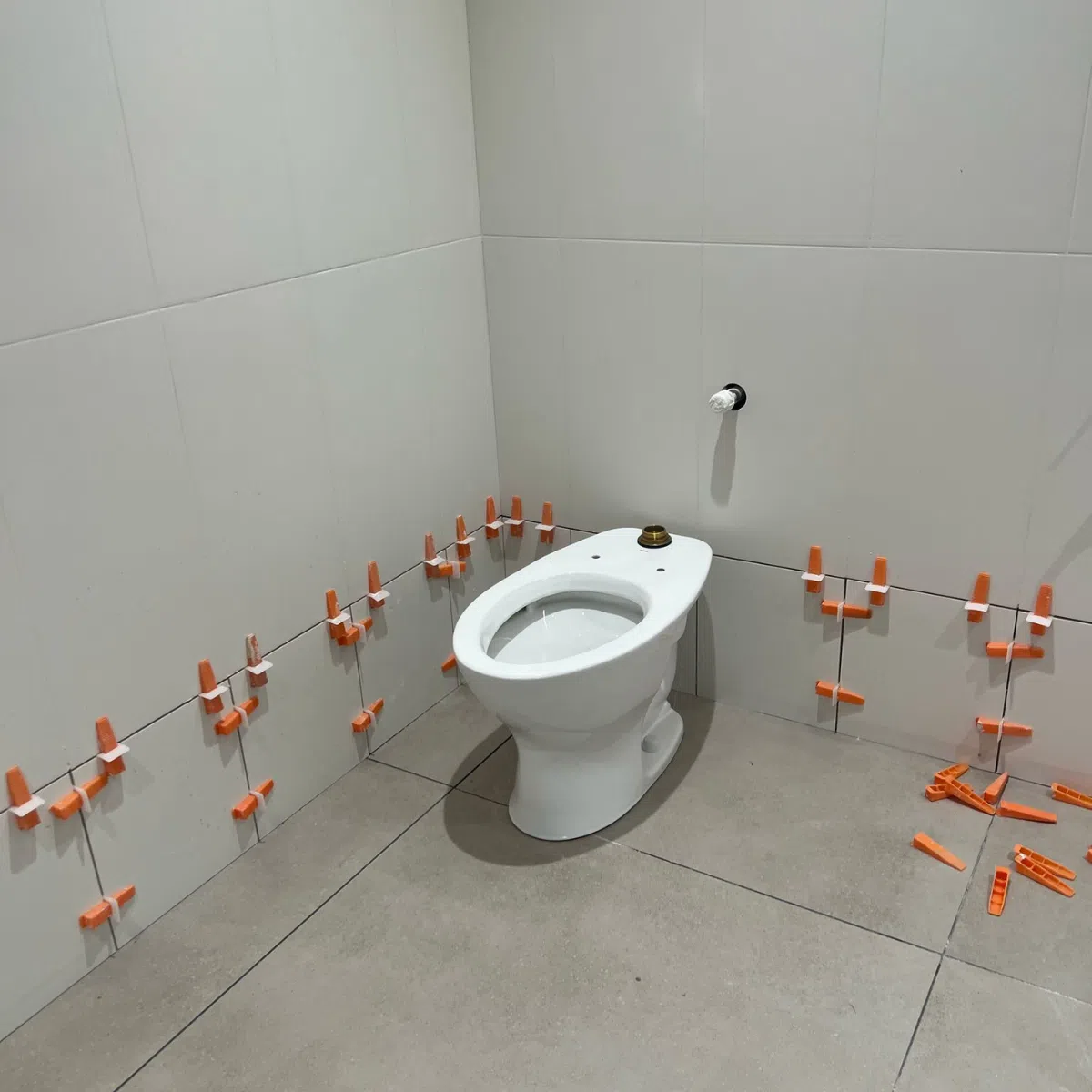 New toilet installation in commercial restroom with freshly installed wall tiles and leveling spacers in place.