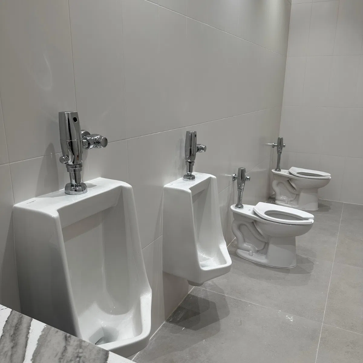 Renovated commercial restroom featuring wall-mounted urinals, toilets, and modern plumbing fixtures.