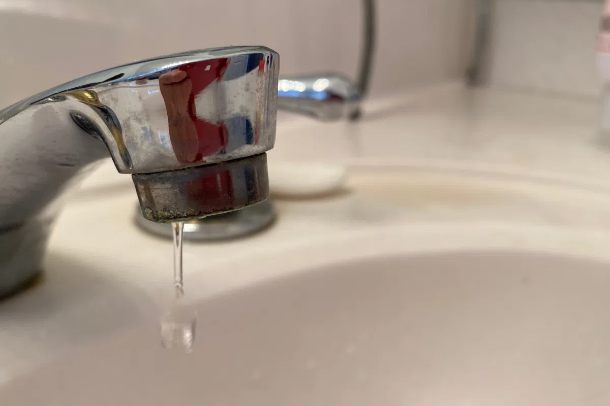 Close-up of a bathroom sink faucet slowly dripping water, illustrating low water pressure or a minor plumbing issue in a residential bathroom.