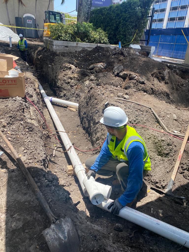 Construction worker installing large PVC sewer pipes in a trench during underground plumbing system installation in Fort Lauderdale.