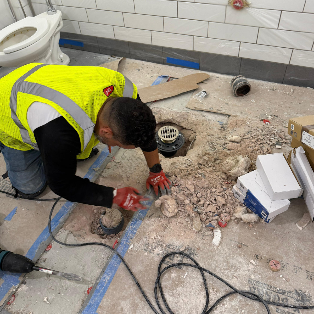 Licensed plumber repairing floor drain and underground plumbing in commercial bathroom renovation project.